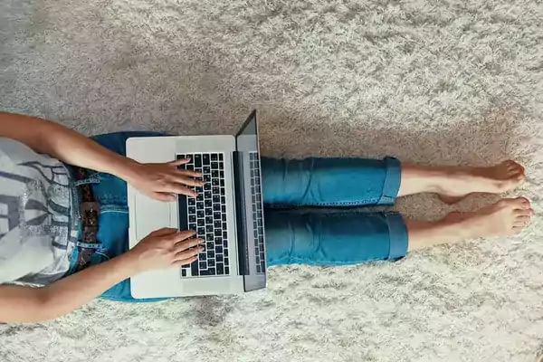 Woman sitting on the floor typing on her laptop.