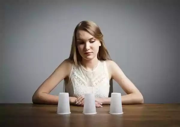 Woman looking at three upside down cups.