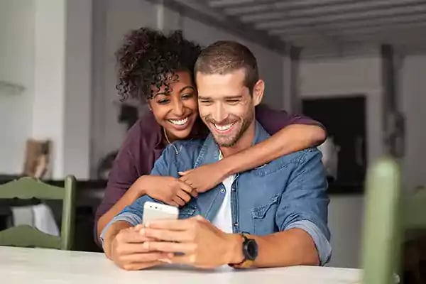 Couple smiling while looking at a phone screen together.