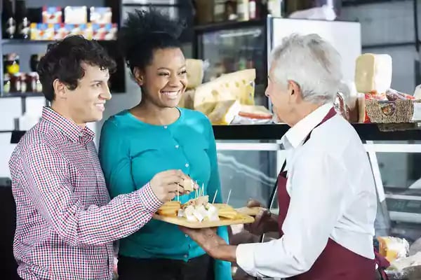 Salesman Offering Cheese Samples To Customers In Shop