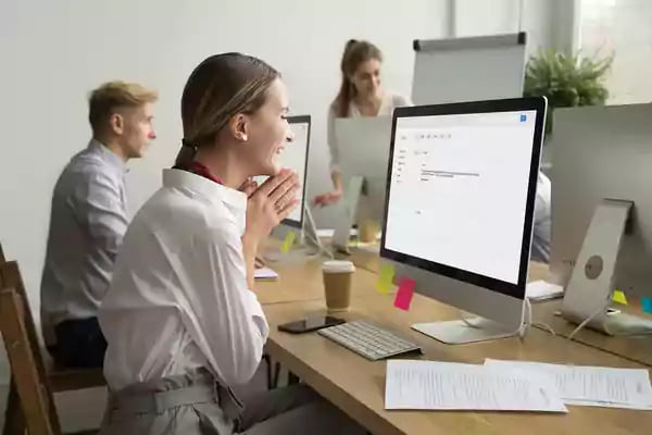 Woman sitting at a desk with a desktop computer smiling.