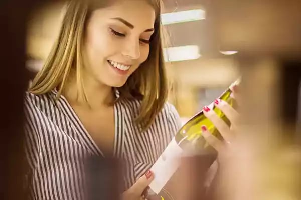 Woman looking at a label on a bottle of wine.