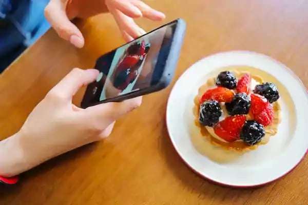 Person taking a picture of a fruit tart.
