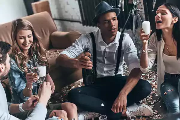 Group of friends sitting on the floor drinking alcoholic beverages.