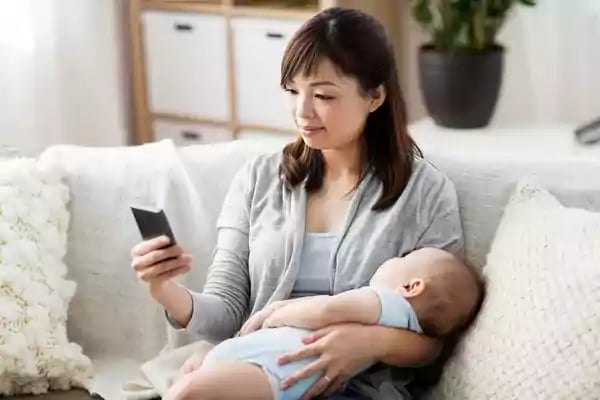 Woman holding a baby while using her phone.