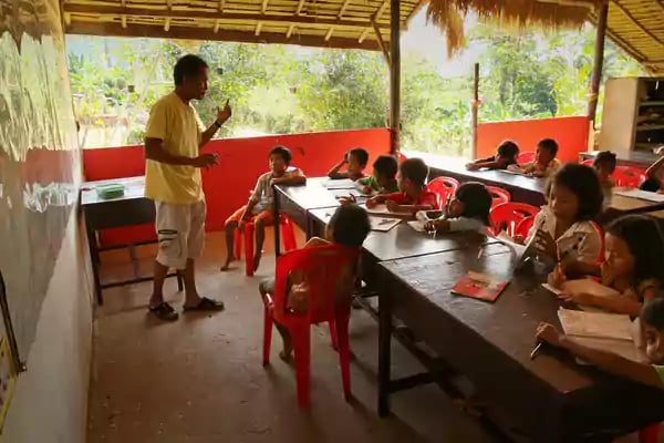Teacher standing in front of class filled with children.