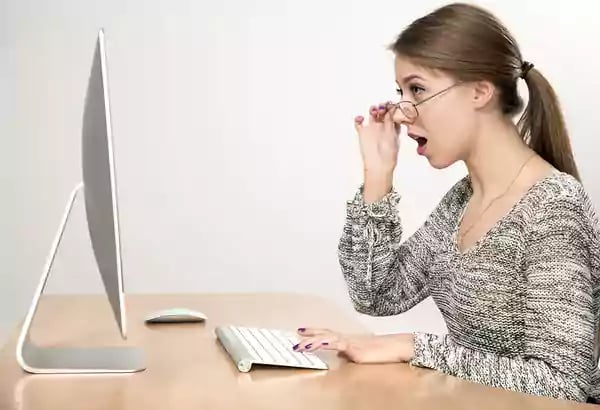 Woman working on a desktop computer looking surprised.