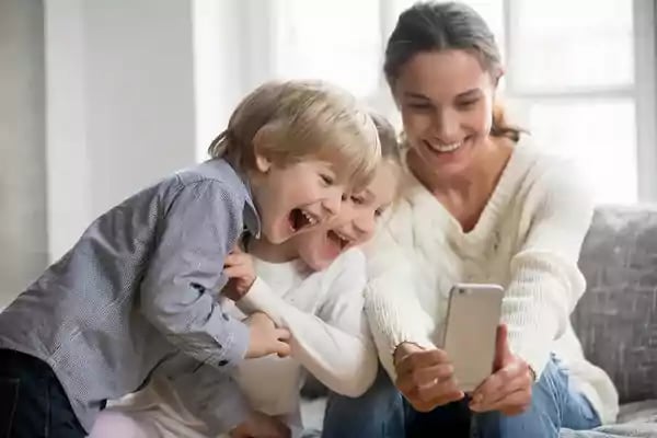 Mother with two children laughing while looking at a mobile phone.