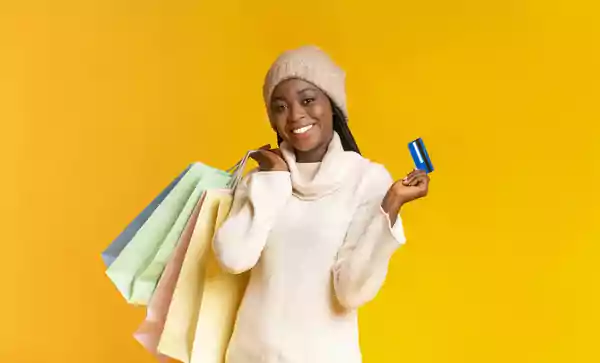 Woman holding shopping bags in one hand and a credit card in the other.