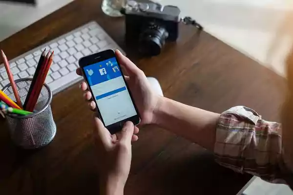 Person holding a mobile phone with the facebook app displaying.