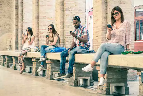 Group of people sitting on a bench looking at their phones.