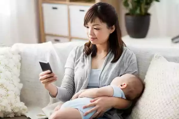 Woman holding a baby while using her phone.