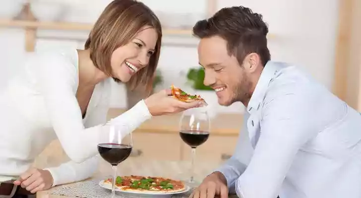 Couple drinking red wine with pizza.