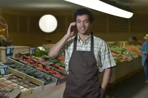 Grocery worker with a brown apron talking on a cell phone.